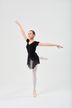 Eine junge Balletttänzerin in einem schwarzen Ballettbody und Rock führt eine Arabeskenpose aus. 3
