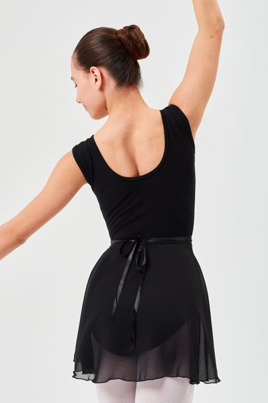 Balletttänzerin in schwarzem Ballettbody und Rock posiert mit erhobenen Armen und blickt von der Kamera weg.