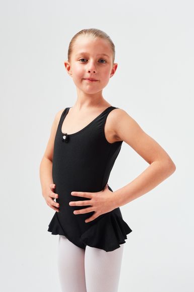 Ein junges Mädchen in einem schwarzen Ballettbody und weißen Strumpfhosen steht mit den Händen in den Hüften.