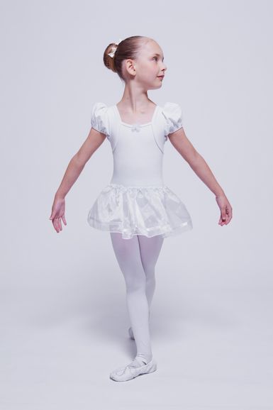 Junges Mädchen in einem weißen Ballett-Outfit posiert in einer Tanzposition.