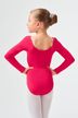 Ein junges Mädchen in einem roten Ballettbody und weißen Strumpfhosen steht mit den Händen in den Hüften und blickt von der Kamera weg. 2