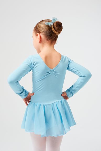 Ein junges Mädchen in einem hellblauen Ballettkleid und einer dazu passenden Haarschleife steht mit den Händen in den Hüften und blickt von der Kamera weg.