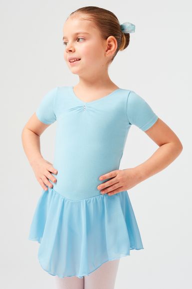 Ein junges Mädchen in einem hellblauen Ballettbody und Rock steht mit den Händen in den Hüften und schaut zur Seite.