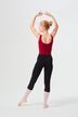 Eine Balletttänzerin in einem roten Trikot und schwarzen Leggings posiert mit erhobenen Armen und dem Rücken zur Kamera.