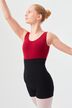 Eine junge Tänzerin in einem roten Trikot mit schwarzen Shorts posiert mit einem erhobenen Arm.