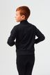 Ein kleiner Junge mit roten Haaren steht mit dem Rücken zur Wand und trägt eine schwarze Jacke und Hose.