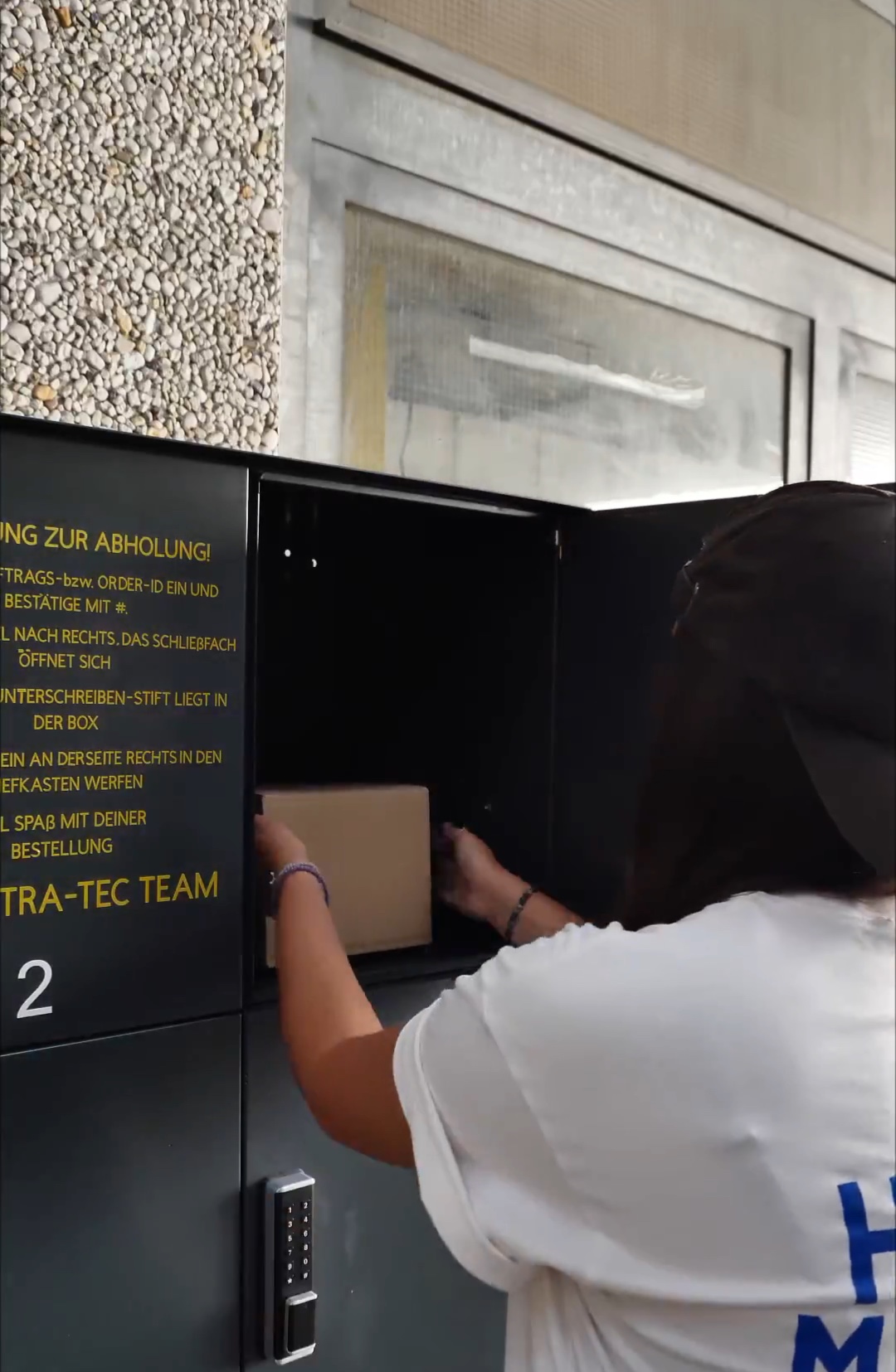 Geöffnete Abholbox mit einem Paket, das eine Person entnimmt.