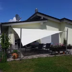 Helles Sonnensegel als Schattenspender über einer Terrasse vor einem modernen Einfamilienhaus.