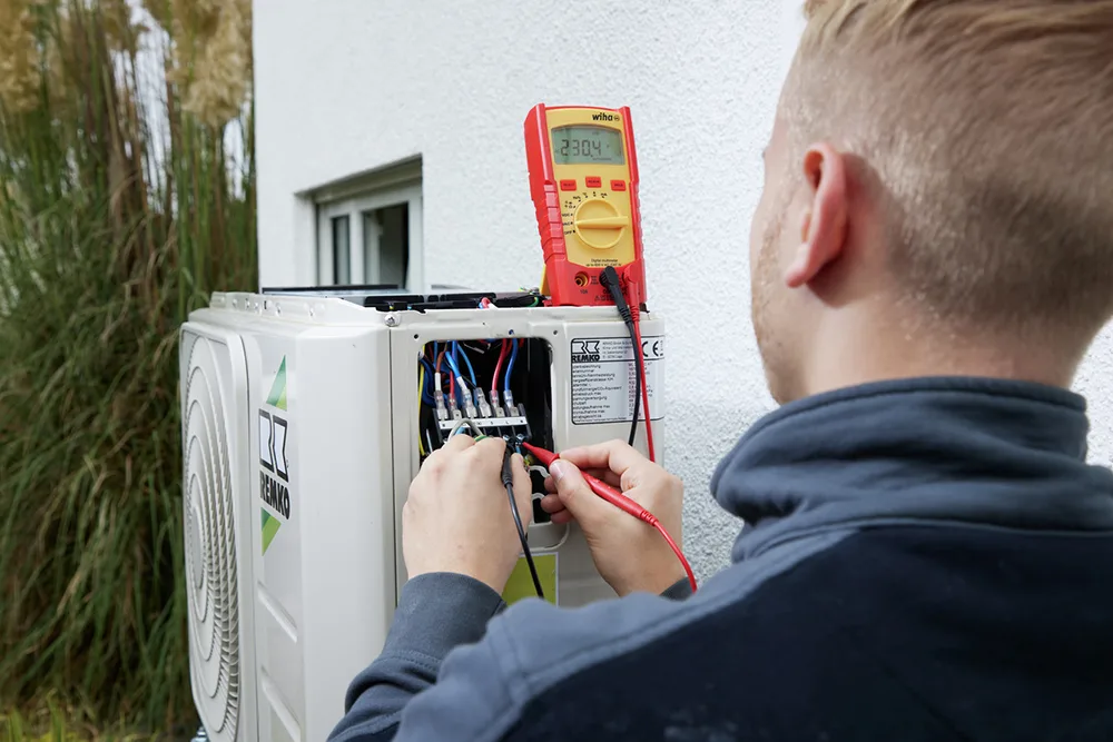 Elektriker misst mit einem Wiha Digitalmultimeter an der Außeneinheit einer Klimaanlage