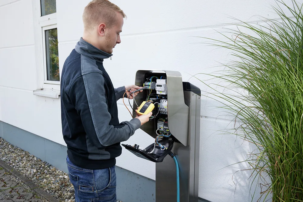 Elektriker prüft eine Ladestation für Elektrofahrzeuge an der Hauswand mit einem Wiha Messgerät