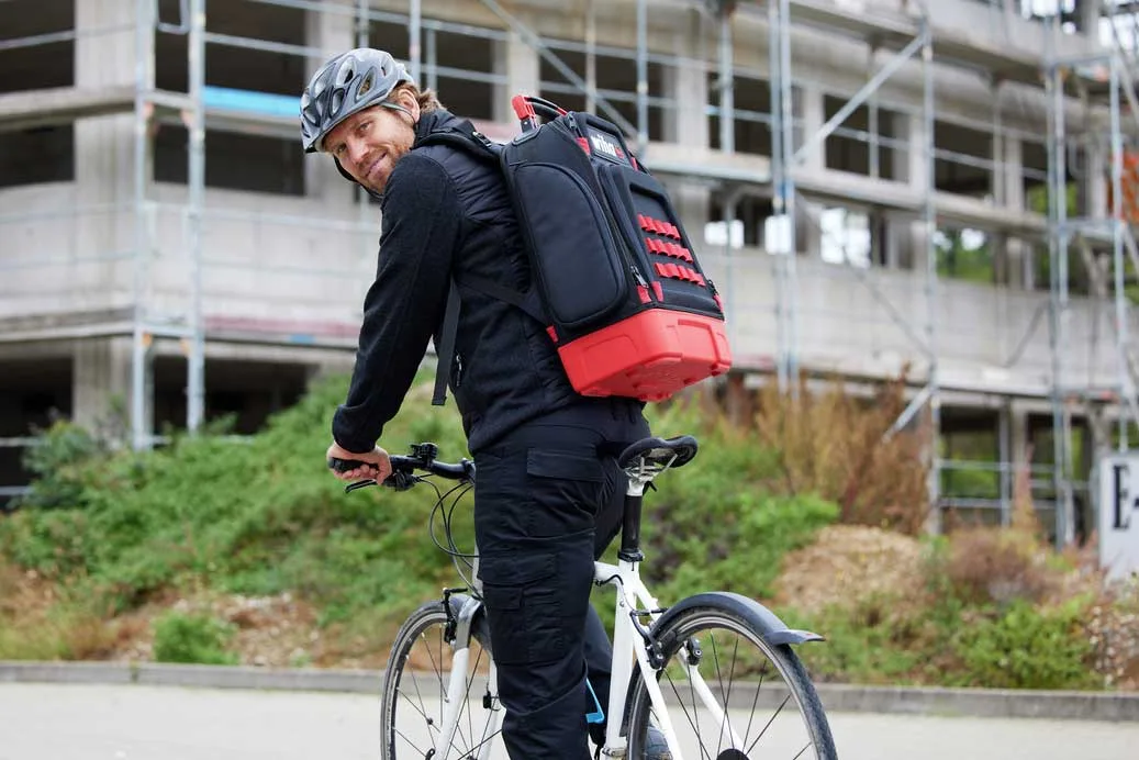Handwerker mit Wiha Werkzeugrucksack auf dem Fahrrad vor einem Rohbau