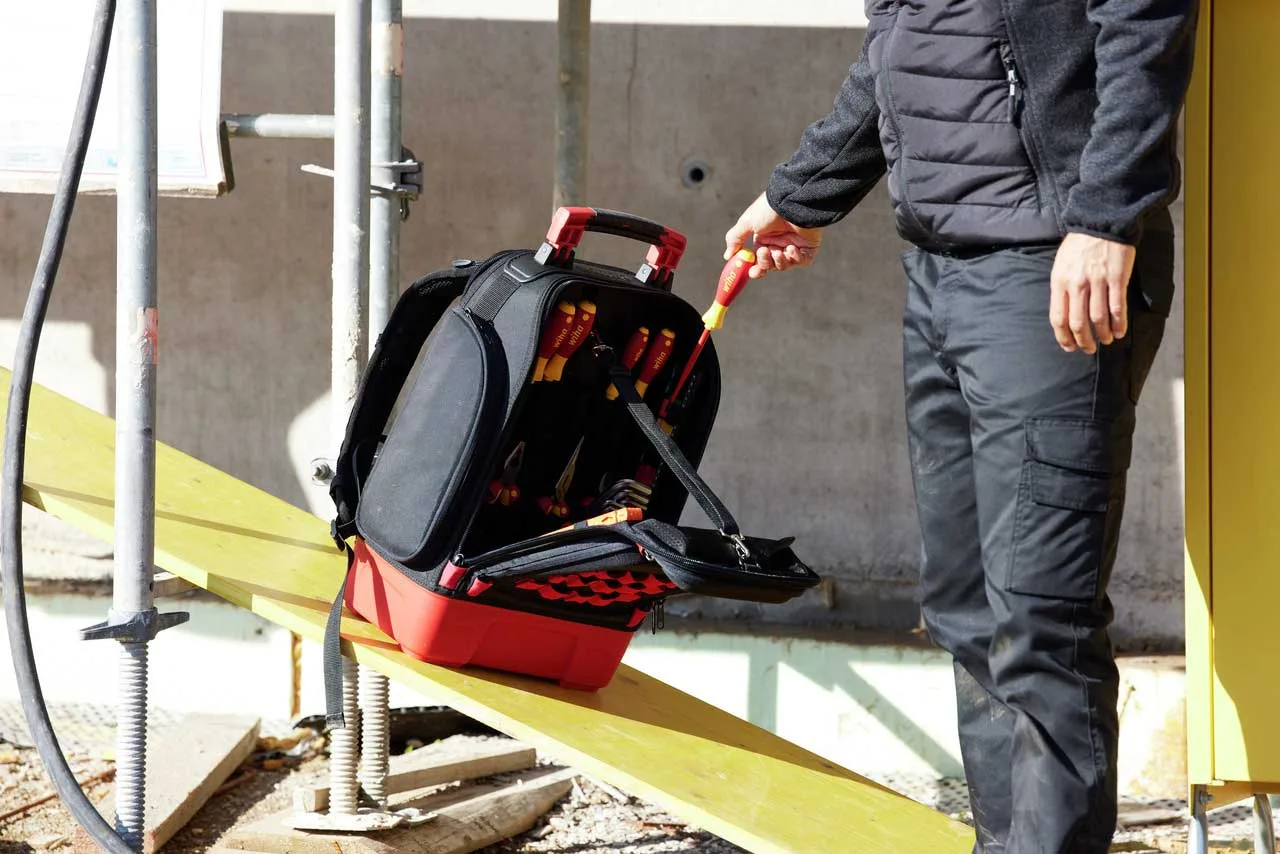 Wiha Werkzeugrucksack mit roter Hartschalen-Wanne steht sicher auf einem Brett, Werkzeug wird entnommen