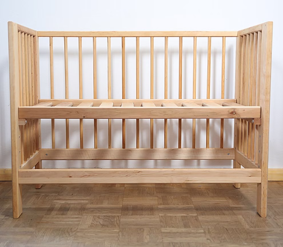 Livipur Livipur Beistellbett Ola aus Bio Erlenholz_2749 Das Livipur Beistellbett Ola aus Bio Erlenholz von Livipur ein leeres Holzbett mit vertikalen Latten an allen Seiten steht auf einem Parkettboden vor einer schlichten weißen Wand und wird ohne Matratze geliefert.