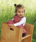 Livipur Livipur Zauberwürfel Hocker 2er Set _3513 Ein kleines Kind mit hellbraunem Haar in einem Pferdeschwanz sitzt seitlich auf einem Livipur Zauberwürfel Hocker (2er Set) von Livipur im Freien trägt eine rot-weiße Latzhose und ein weißes Hemd lächelt und blickt zur Seite.