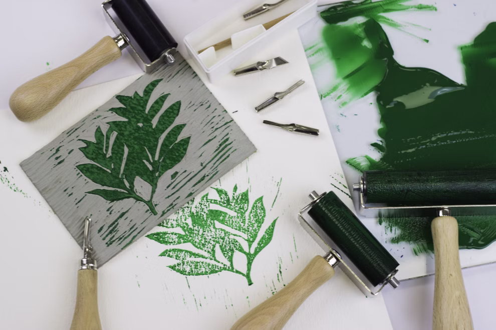 Daler-Rowney Professional Linolplatte A4 Daler-Rowney Professional _14085 Das Daler-Rowney Professional Linolplatte A4-Set enthält Schnitzwerkzeuge eine Walze grüne Tinte und einen geschnitzten Block mit einem Blattmuster sowie ein gedrucktes grünes Blattmuster auf weißem Papier.