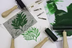 Daler-Rowney Professional Linolplatte A3 Daler-Rowney Professional _14088 Ein Daler-Rowney Professional Linolplatte A3 Drucksetup mit Schnitzwerkzeugen Walzen grüner Tinte einem geschnitzten Linoleumblock mit einem Blattmotiv und dem resultierenden Blattdruck auf weißem Papier.