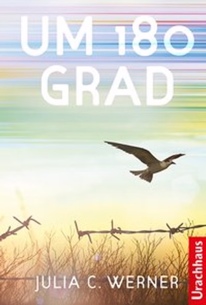 Urachhaus Um 180 Grad Julia C. Werner_8270 Das Buch Um 180 Grad von Julia C. Werner zeigt unter dem Titel einen fliegenden Vogel in der Nähe von Stacheldraht vor einem Himmel mit bunten horizontalen Streifen. Der Markenname Urachhaus ist ebenfalls auf dem Cover zu sehen.