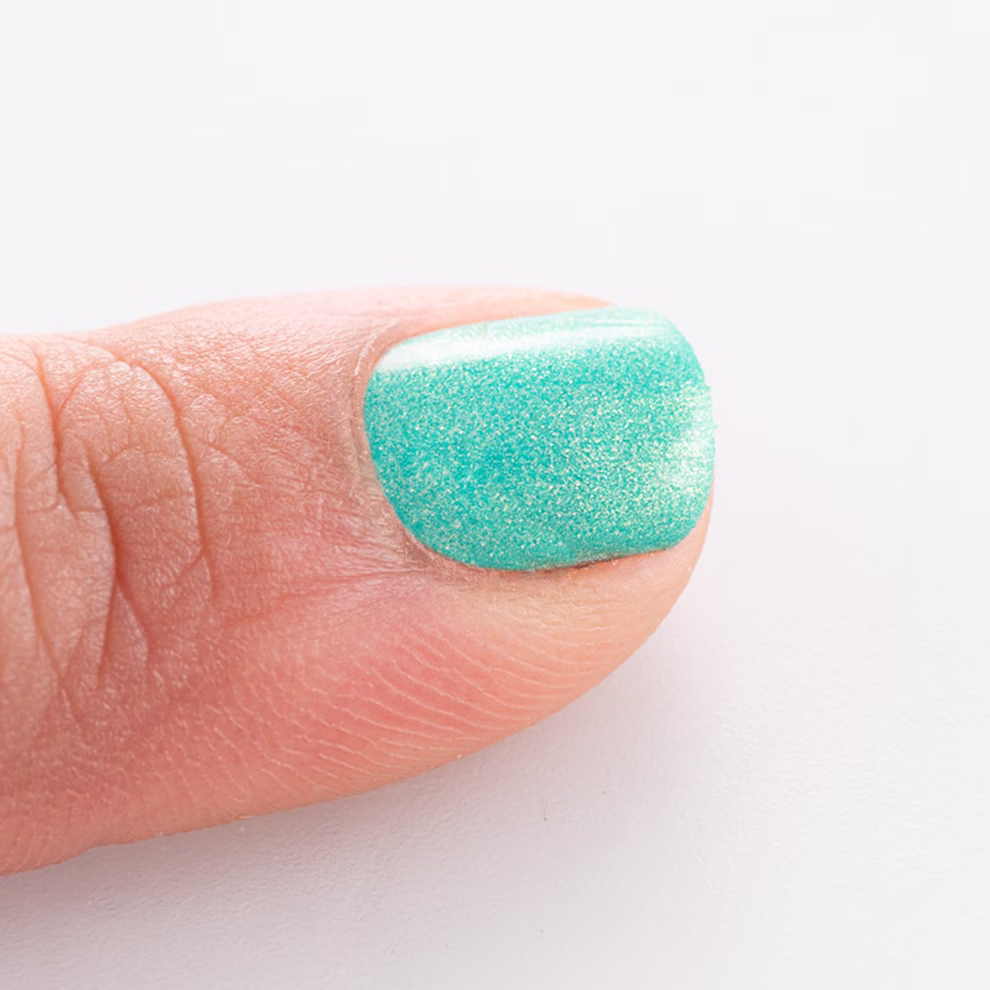 Namaki Cosmetics Nagellack auf Wasserbasis in verschiedenen Farben _25303 türkis Nahaufnahme eines Daumens mit dem türkis schimmernden Nagellack auf Wasserbasis in verschiedenen Farben von Namaki Cosmetics vor einem weißen Hintergrund. türkis