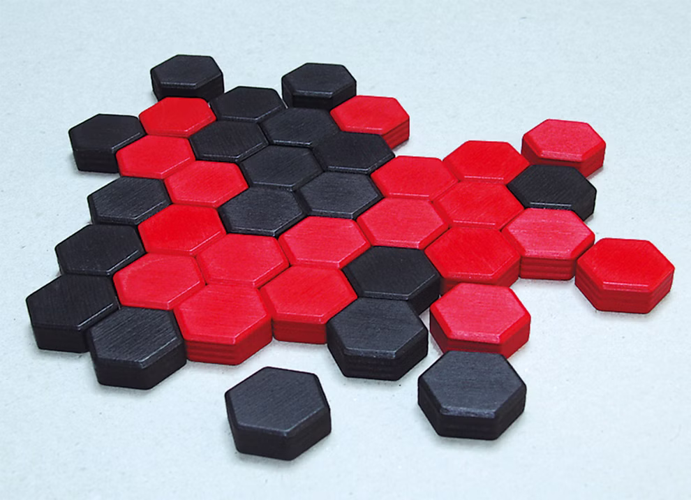 Steffen Spiele Spiel - Six Das raffinierte Legespiel_16624 Sechseckige rote und schwarze Teile aus Steffen Spiele's Spiel - Six Das raffinierte Legespiel sind auf einer hellen Fläche ineinander verschachtelt und bilden ein abstraktes fischähnliches geometrisches Muster.