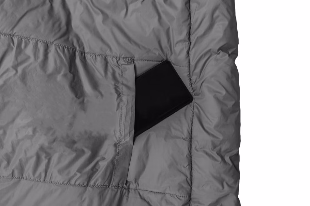 Schlafsack mit Almwolle Ein Schlafsack mit Almwolle von Grüezi bag passend für Körpergrößen bis 185 cm liegt teilweise im geöffneten grauen Packsack vor weißem Hintergrund.