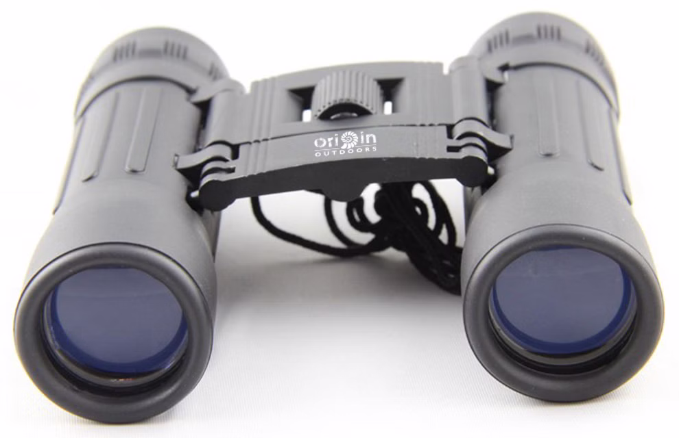 Origin Outdoors Fernglas 10-fache Vergrößerung_18196 Die Origin Outdoors Fernglas 10-fache Vergrößerung ist ein schwarzes Kompaktfernglas mit blau getönten Linsen zentralem Fokussierrad und Umhängeband das auf einer weißen Fläche liegt.