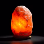 Die Himalaya Salt Dreams Salzkristalllampe mit Holzsockel (mittel ca. 2-3 kg) leuchtet in orange-rosa Tönen auf einem kleinen Holzsockel vor dunklem Hintergrund.