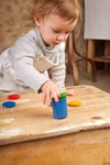 Grapat Grapat Holzspielzeug 6 Becher mit Deckel bunt _19420 Ein kleines Kind spielt mit dem Grapat Holzspielzeug 6 Becher mit Deckel bunt von Grapat stellt einen bunten Holzbecher auf den Tisch und konzentriert sich auf die Tätigkeit.