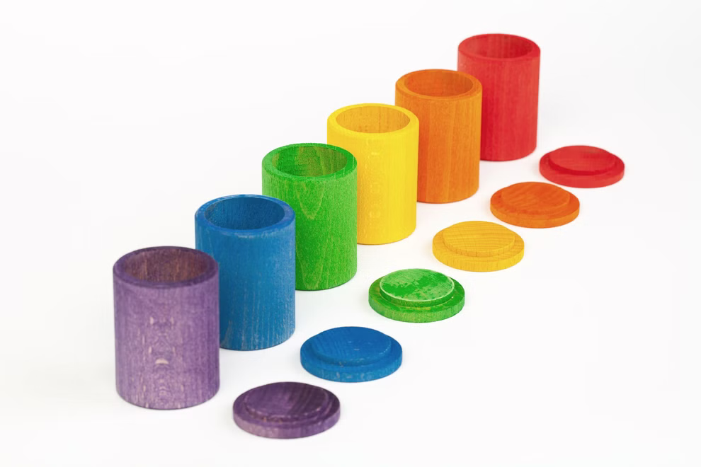 Grapat Grapat Holzspielzeug 6 Becher mit Deckel bunt _19418 Das Grapat Holzspielzeug 6 Becher mit Deckel bunt von Grapat besteht aus sechs bunten Holzbechern mit passenden flachen Deckeln in den Farben lila blau grün gelb orange und rot die in einer Reihe auf einem weißen Hintergrund angeordnet sind.