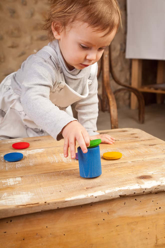 Grapat Grapat Holzspielzeug 6 Becher mit Deckel bunt _19420 Ein kleines Kind spielt mit dem Grapat Holzspielzeug 6 Becher mit Deckel bunt von Grapat stellt einen bunten Holzbecher auf den Tisch und konzentriert sich auf die Tätigkeit.
