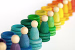Grapat Große Holzbox Holzpuppen und Ringe von Grapat sind auf einem weißen Hintergrund in einem Regenbogenmuster mit Farbverlauf von blau und grün bis gelb und orange angeordnet.