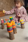 Ein junges Mädchen sitzt in einem gemütlichen Zimmer auf dem Boden und stapelt bunte Grapat Große Holzbox Holzringe und Steckpuppen von Grapat auf Baumstumpfblöcken.