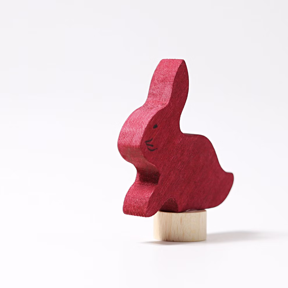 Grimm's Grimm`s Steckfigur Hase _19794 Die Grimm'sche Steckfigur Hase ist ein kleiner roter Holzhase mit einfachen schwarzen Gesichtszügen der auf einem kurzen runden hellen Holzzylinder balanciert und vor einem schlichten weißen Hintergrund abgebildet ist.