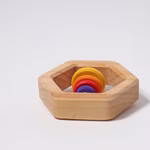 Grimm's Sechseck Rassel Ø 8 cm von Grimm's ist ein sechseckiges Holzspielzeug mit vier bunten kreisförmigen Scheiben (gelb orange rot und lila) die im Inneren gestapelt sind und auf einem schlichten weißen Hintergrund abgebildet sind.