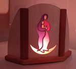 Die Adventsleuchte Motiv Din A6 von Decor ist eine Holzleuchte mit einer stilisierten Figur die ein Kind im Arm hält das von hinten sanft mit rosafarbenem Licht beleuchtet wird und einen warmen sanften Schein abgibt. Maria auf Sichel