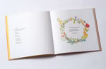 Mummel & Hummel Malwerkstatt Wunderbare Winzigkeiten Ein Spaziergang durchs Jahr_22385 Das aufgeschlagene Buch "Wunderbare Winzigkeiten Ein Spaziergang durchs Jahr" von Mummel & Hummel Malwerkstatt zeigt auf der linken Seite einen Text und auf der rechten Seite einen farbenfrohen Blumenkranz der ein deutsches Zitat einrahmt alles auf einem w