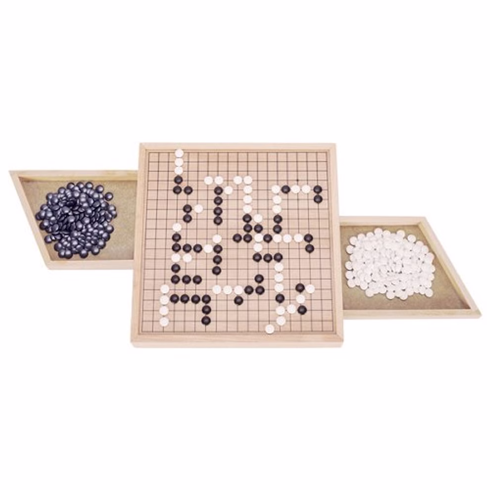 Goki Go Brettspiel mit Ausziehfächern_26470 Das Goki Go Brettspiel mit Ausziehfächern ist mit einem laufenden Spiel abgebildet; das Holzbrett liegt zwischen zwei ausziehbaren Tabletts von denen eines schwarze und das andere weiße Steine enthält alles vor einem weißen Hintergrund.