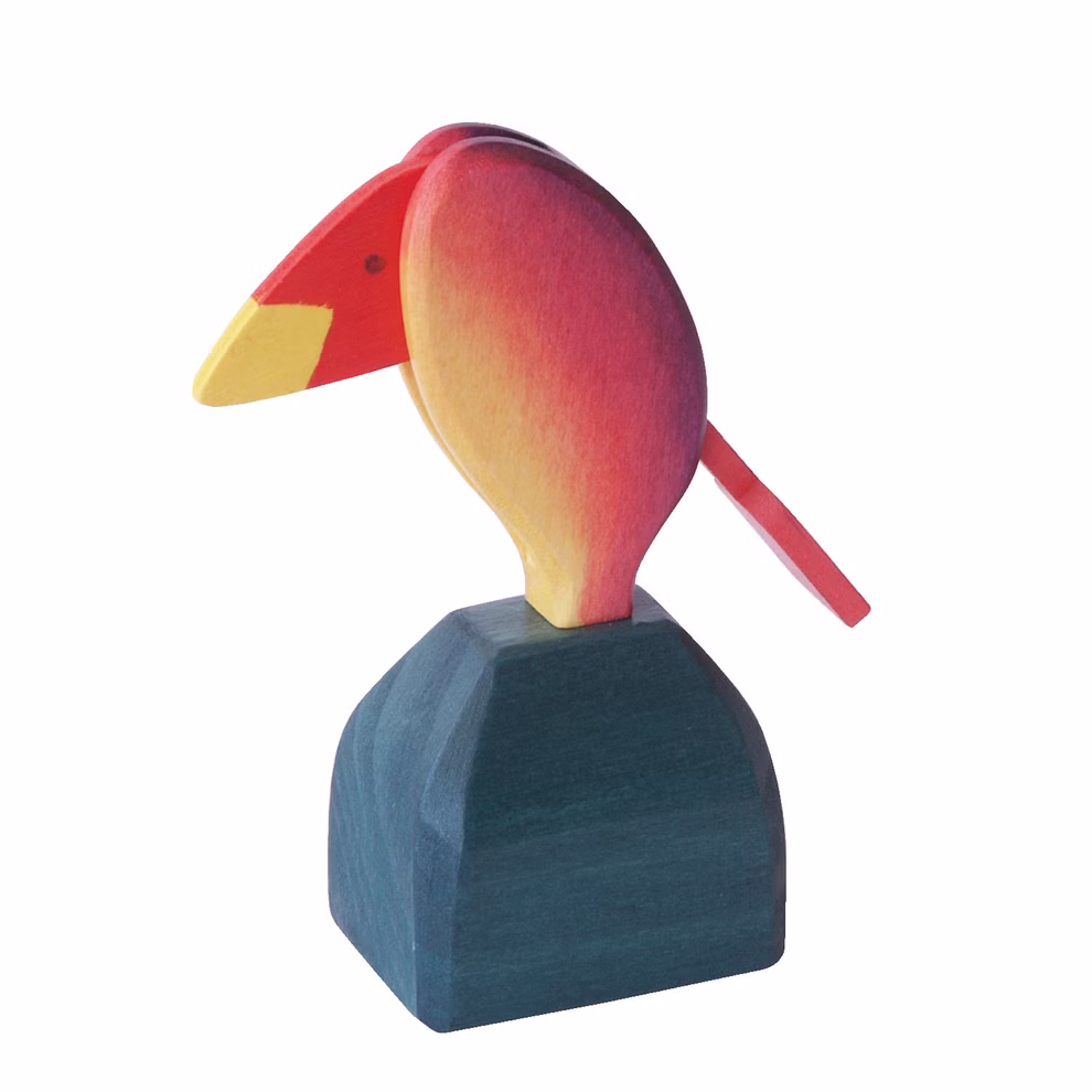 Decor Stimmungsvogel Temperamentsvogel _314 Der Decor Stimmungsvogel Temperamentsvogel ist ein hölzerner Spielzeug-Tukan mit gelbem Schnabel rotem Kopf und orange-roten Flügeln der auf einem blau-grünen Sockel sitzt.