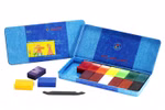 Eine blaue Stockmar-Blechdose mit deutscher Beschriftung enthält 16 bunte Stockmar Wachsmalblöcke. Einige Blöcke und ein schwarzer Spachtel befinden sich außerhalb der Dose. Auf dem Deckel ist eine Kinderzeichnung zu sehen.