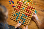 Ein Kind und ein Erwachsener spielen das Farbenspiel 10x10 von Romanswerk und legen blaue und rote Filzkugeln in das mit 100 bunten Filzkugeln gefüllte Holzgitter.