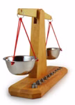 Die Decor Waage mit zehn Gewichten Holzwaage zeigt eine Holzwaage mit zwei an roten Schnüren hängenden Metallschalen und einer Reihe von zehn Metallgewichten auf dem Holzsockel.