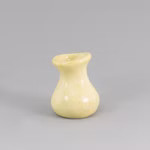Die Lautenbach "Vase in vier Farben" ist eine kleine glänzende blassgelbe Keramikvase mit breitem abgerundetem Körper schmalem Hals und ausgestelltem Rand die vor einem schlichten grauen Hintergrund gezeigt wird. gelb pastell