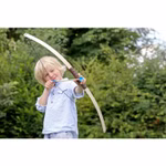Spielzeugmanufaktur VAH Pfeil und Bogen L 100 cm_1335 Ein zielstrebiges Kind im hellblauen Hemd zielt mit der Spielzeugmanufaktur VAH "Pfeil und Bogen L 100 cm" im Freien vor grünen Büschen und Bäumen stehend die blonden Haare nach hinten gezogen bereit den Pfeil abzuschießen.