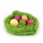 Ein grünes flauschiges Nest zeigt die Eier von ökoNORM Natur Eierfarben 5 Farben - gelb rosa orange rot und grün - vor einem schlichten weißen Hintergrund.