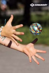 Schildkröt High Bounce Balls (Flummies) 3-er Set _26506 Zwei ausgestreckte Hände greifen im Freien nach einem farbenfrohen High Bounce Ball aus dem Schildkröt Flummies 3er-Set mit dem Schildkröt-Logo in der rechten oberen Ecke.