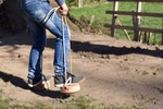 Jamso Design Shaddy Hufe _26705 Eine Person geht mit Jeans und Turnschuhen auf den Shaddy Hufe Stelzen von Jamso Design über einen sandigen Boden mit Gras und einem Holzzaun.