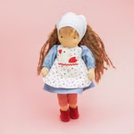 Die Käthe Kruse Waldorfpuppe Tilda 38 cm ist eine handgefertigte Stoffpuppe mit langen braunen Haaren bekleidet mit einem blauen Kleid einer Hühnerschürze rot-weiß gestreiften Leggings roten Schuhen und einem blau-karierten Kopftuch posiert vor einem rosa 
