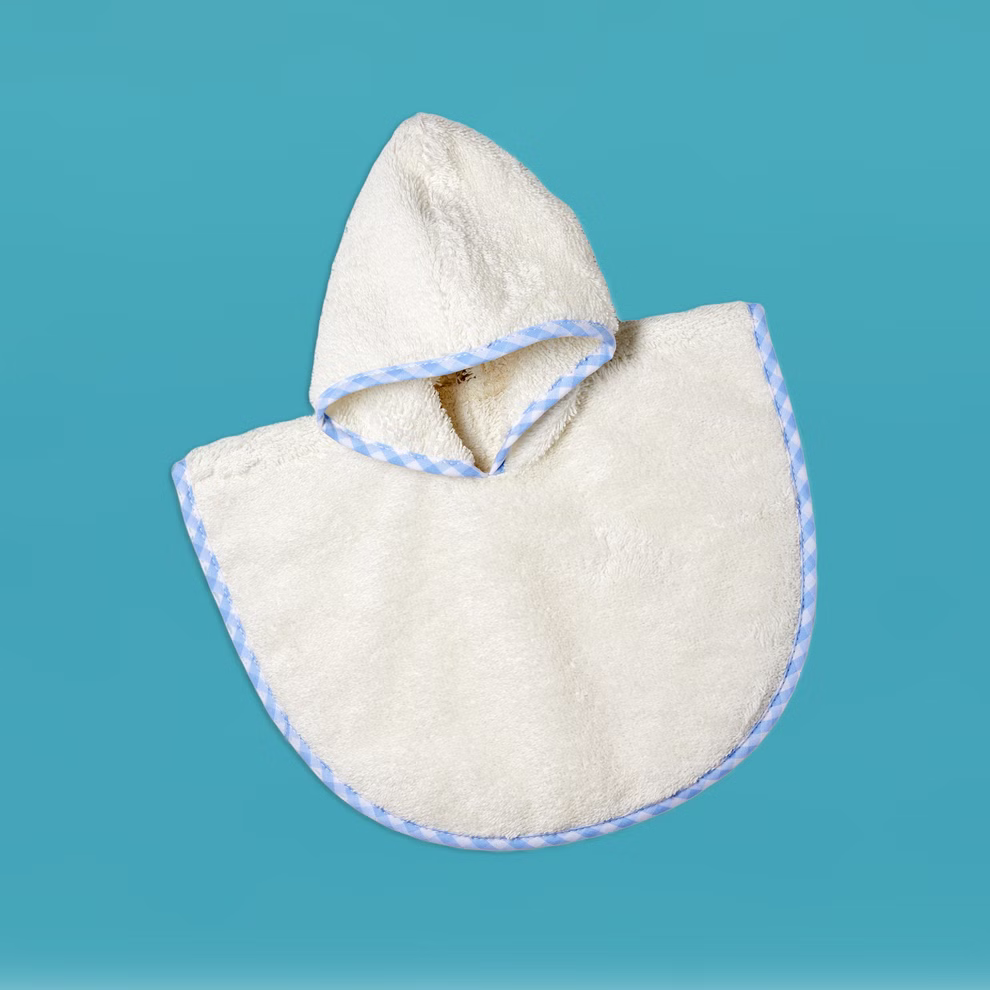 Käthe Kruse Badeponcho für Waldorfpuppen für Puppen der Größe 28-35 cm _26165 Das Käthe Kruse Badeponcho für Waldorfpuppen (für Puppen 28-35 cm) ist ein weißes Kapuzenhandtuch mit blauem Rand halbkreisförmig flach auf blauem Hintergrund mit der Kapuze oben in der Mitte.