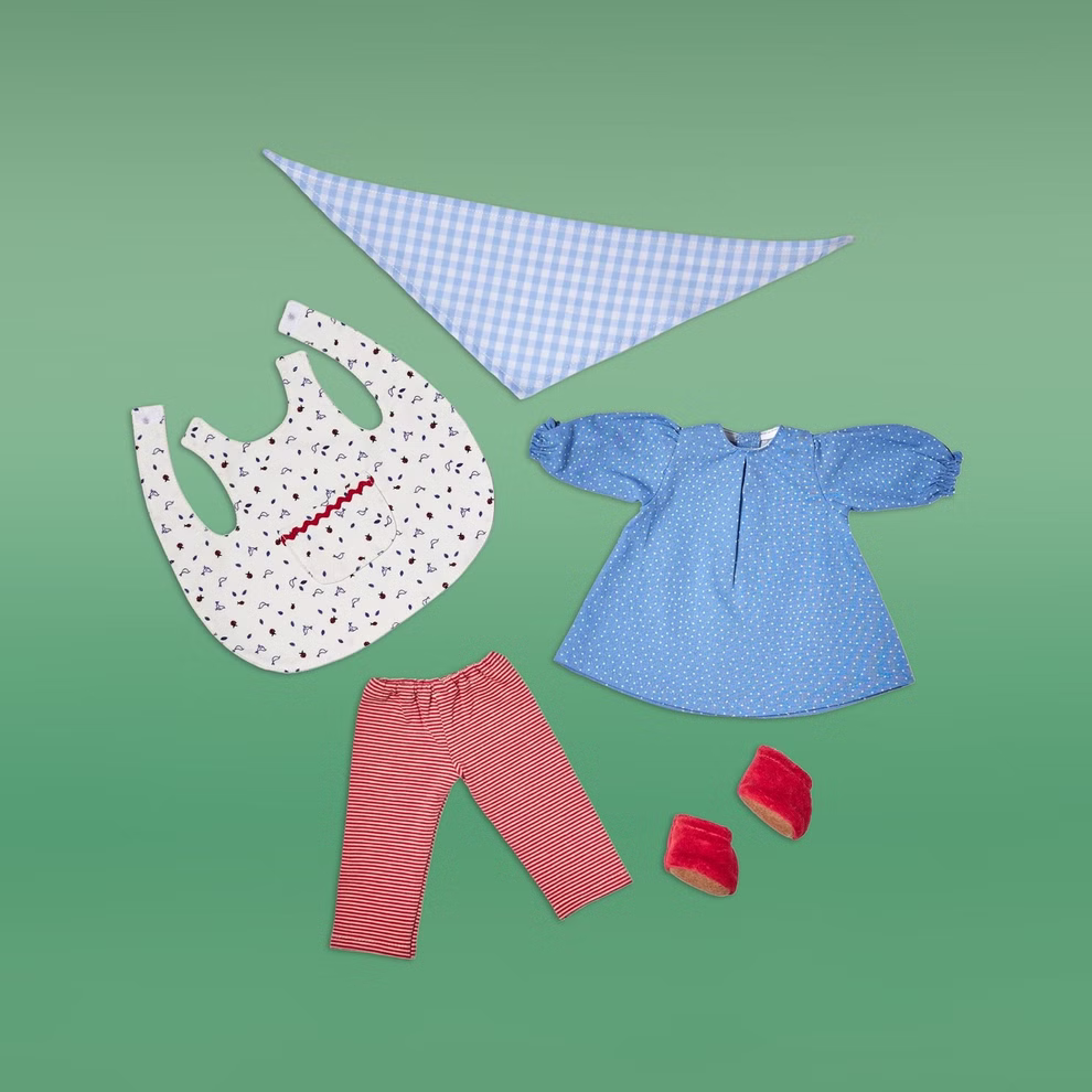 Käthe Kruse Kleidungsset Tilda Puppenbekleidung _26161 Das Käthe Kruse Kleidungsset Tilda Puppenbekleidung besteht aus einem blau gemusterten Kleid einer rot-weiß gestreiften Hose einem gemusterten Lätzchen einem blau-weiß karierten Schal und roten Schuhen - alles auf grünem Hintergrund.