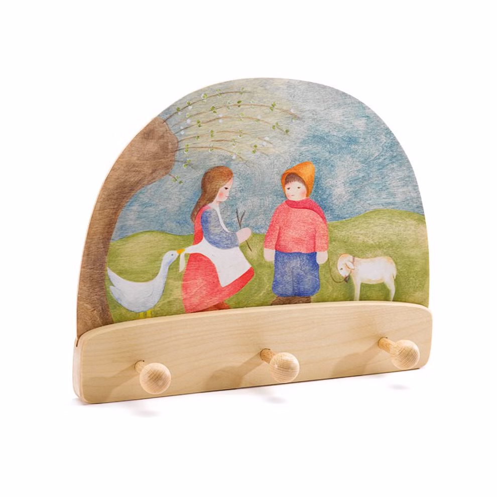Ostheimer Ostheimer Garderobe Hirtenkinder _26815 Ostheimer Garderobe Hirtenkinder von Ostheimer ist ein hölzerner Wandhaken mit drei Haken der eine gemalte Szene mit Kindern einer Gans und einem Lamm unter einem Baum vor einem blauen Himmel zeigt.