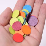 Grimm's Konfettitaler Regenbogen aus Holz _28816 Eine Hand hält mehrere Grimm'sche Konfettitaler Regenbogen aus Holz - kleine runde bunte Holzteile in den Farben Rot Orange Gelb Grün Blau und Violett die auf der Handfläche verstreut sind.